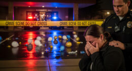 A heartbreaking scene outside a banquet hall in Stockton at night, with police lights reflecting on yellow crime scene tape. A grieving parent is comforted by a police officer in the foreground.